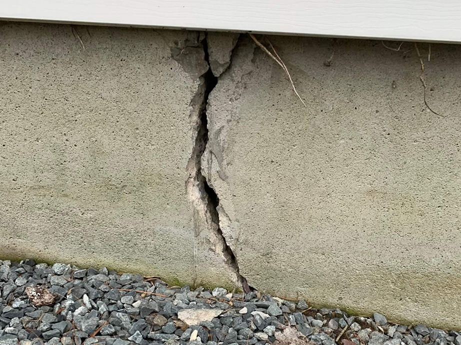 large foundation crack at base near landscaping with debris